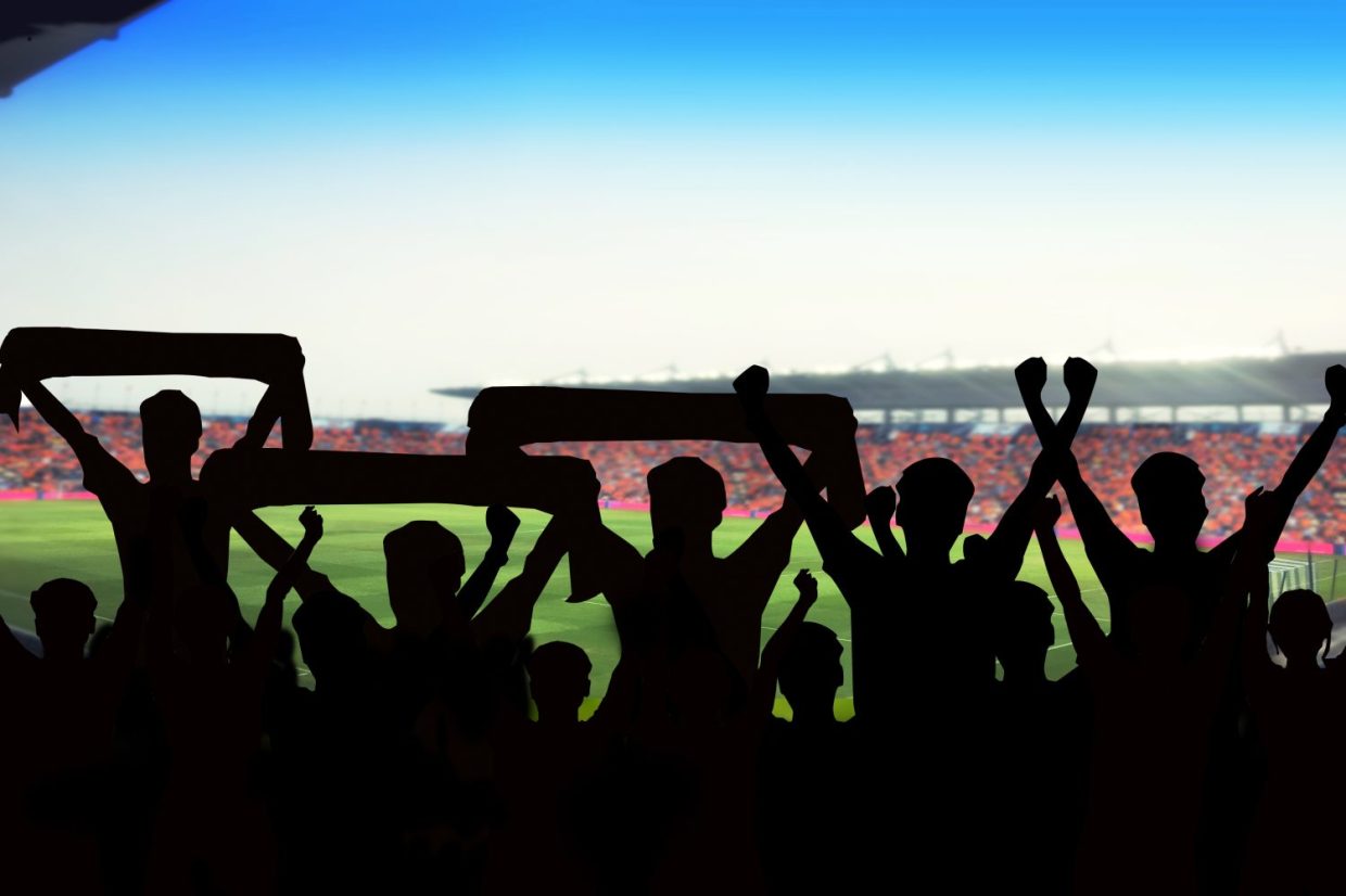 Silhouettes of soccer fans standing and cheering.