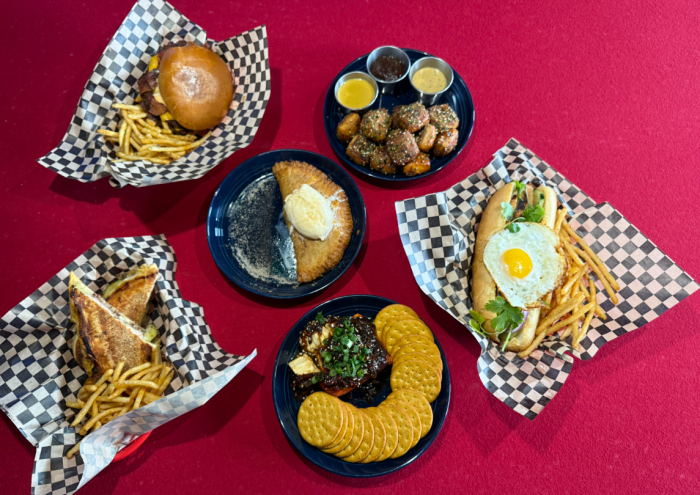 Rising Tides dishes, including a dessert empanada and smash burger, laid out over a pool table.