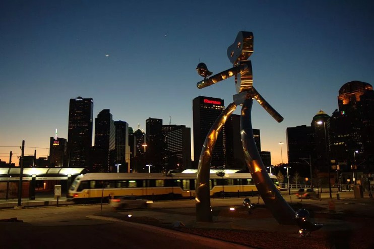 Chrome traveling man robot statue in deep ellum with dart train and Downtown Dallas skyline in background