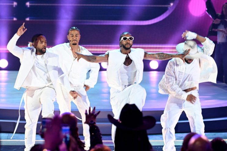 members of b2k are dressed in all-white outfits on stage with a purple backdrop at the BET awards