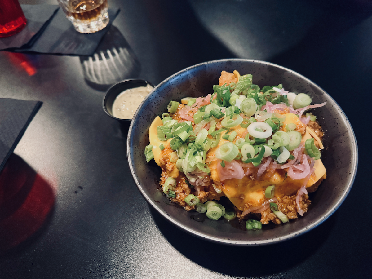 A close up of a bowl of chicken nuggets topped with cheese and green onions.