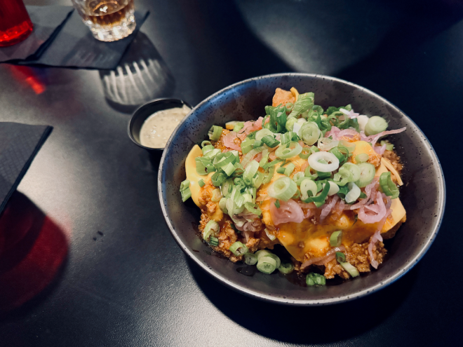 A close up of a bowl of chicken nuggets topped with cheese and green onions.