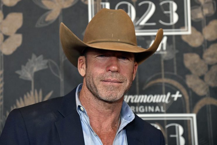 Taylor Sheridan wears brown cowboy hat in front of press step and repeat for paramount plus