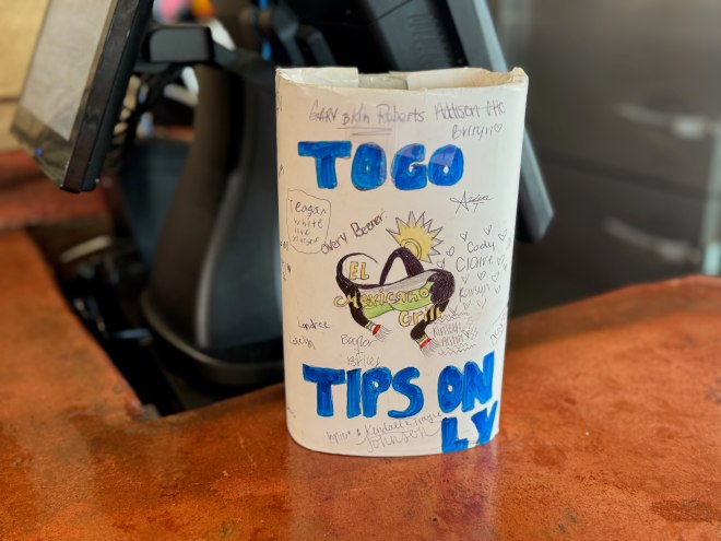 A brightly colored to-go tip jar on a counter of a restaurant.