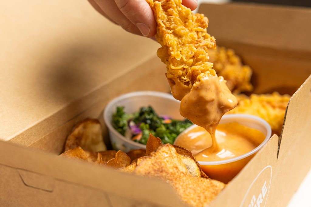 a chicken tender being dipped in a Flock Sauce