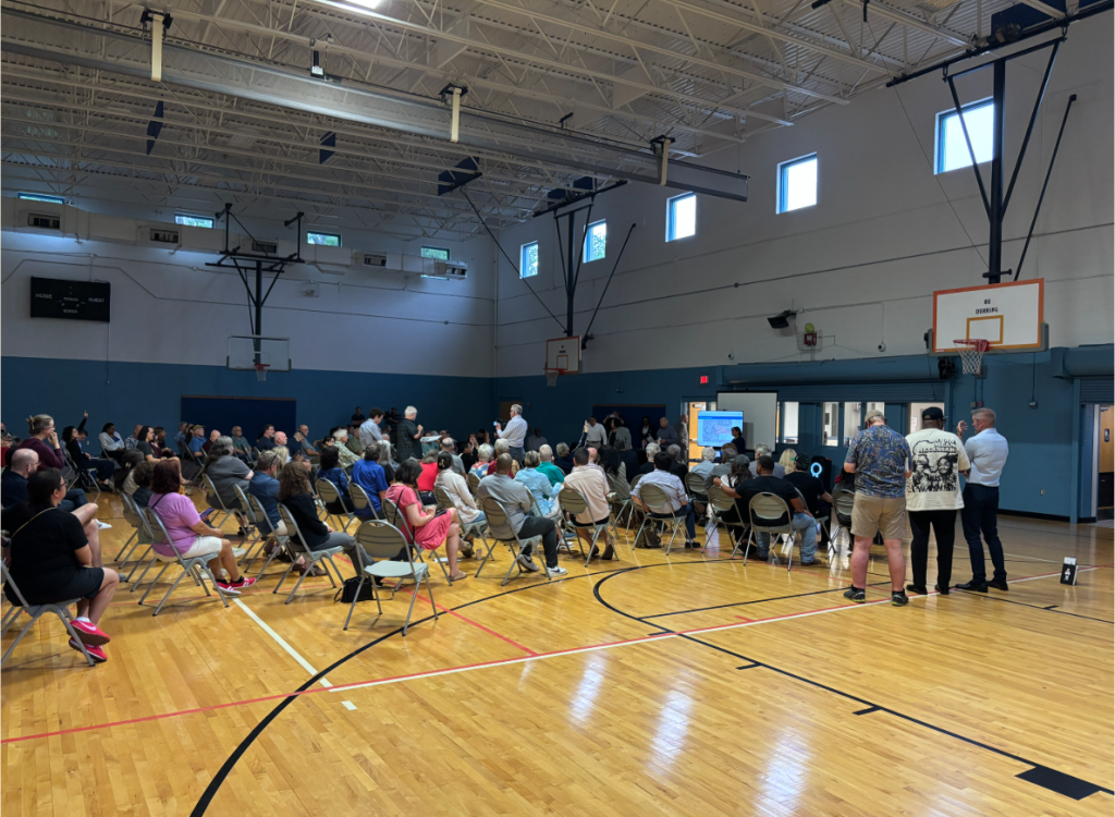 Oak Cliff community meeting in large gym, with the TV in the background.