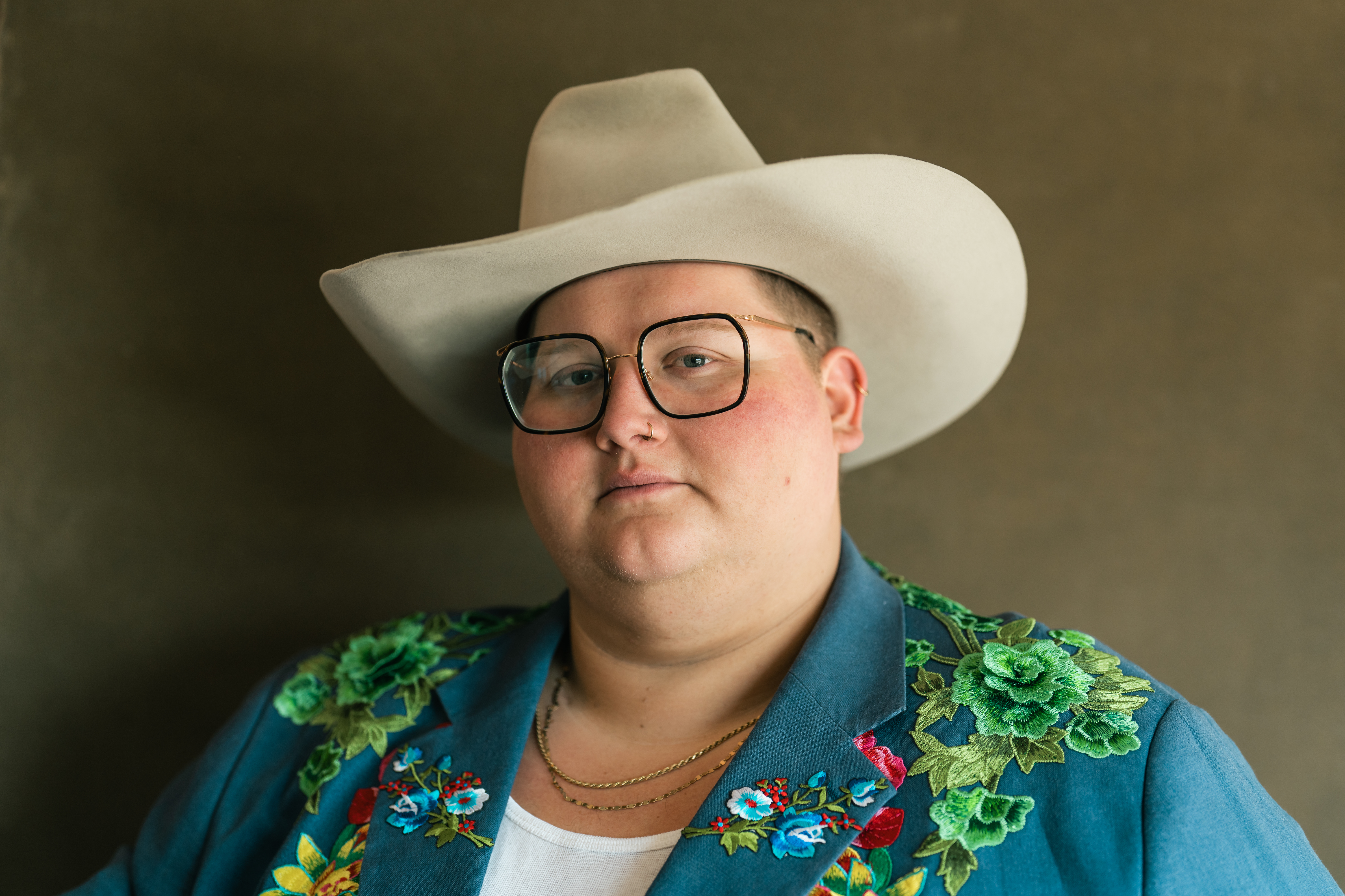 joshua ray walker looks into the camera wearing a white cowboy hat, glassses and an embroidered turquoise blazer
