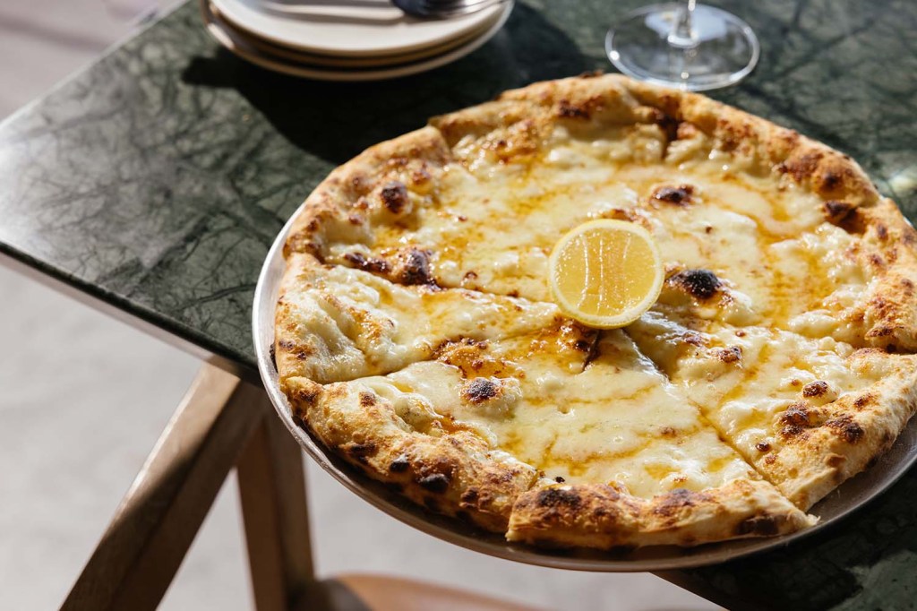 Wood-fired white pizza topped with melted cheese and a lemon slice, served on a metal platter over a dark marble table.