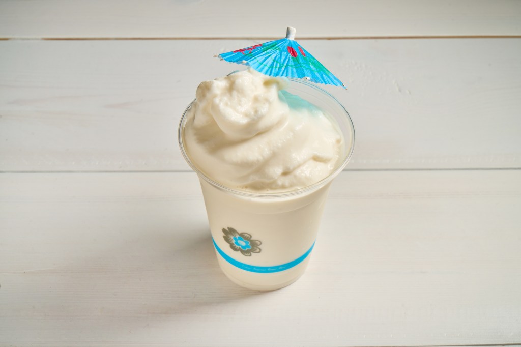 A signature batido from Frita Batidos, served in a clear cup and garnished with a blue paper umbrella.