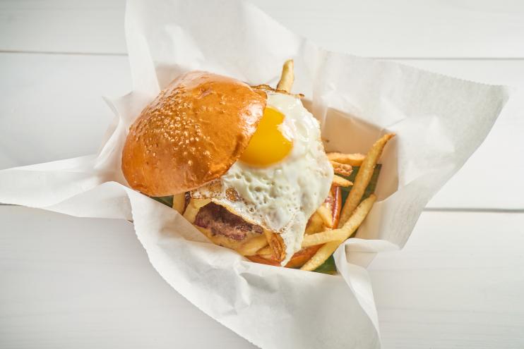 Frita Batidos chorizo burger topped with a fried egg and crispy shoestring fries on a toasted bun, served in a paper-lined basket.