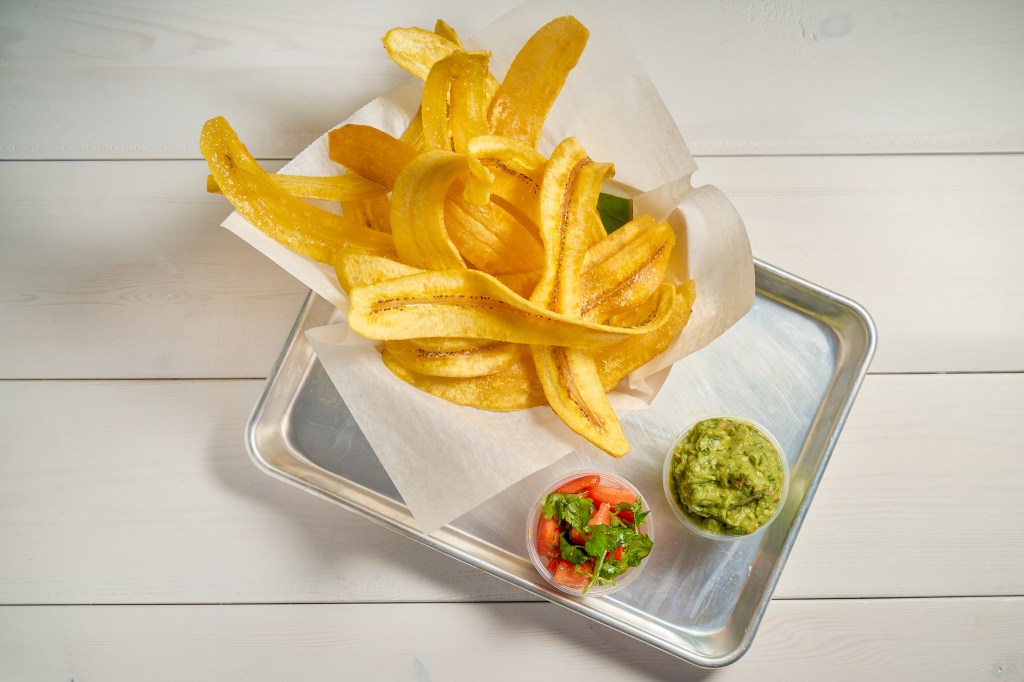 Golden fried sweet plantains arranged in a paper-lined basket on a white table, served as a Cuban-inspired side dish.