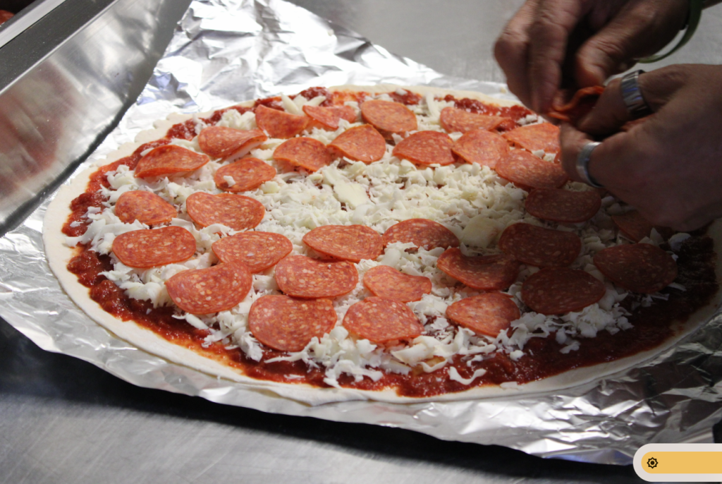 Frankie Nuccio lays sauce, shredded provolone and pepporonis over dough before placing in the oven.