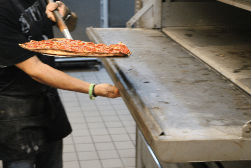 Nuccio pulls a pepperoni pizza from Ghost Pizza's oven.