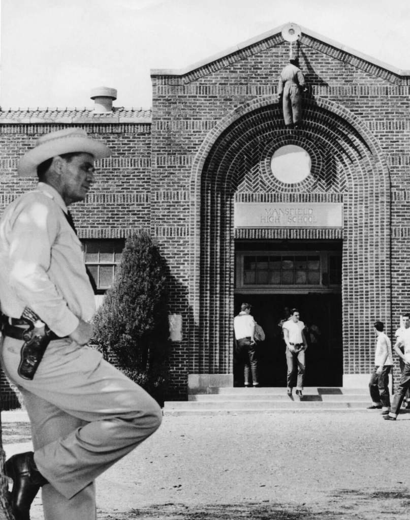 Texas Ranger Jay Banks leans against tree in foreground while black effigy hangs over the entrance to Mansfield High School, during the September 1956 Mansfield Crisis over desegregation.