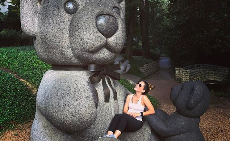 A woman sits on a teddy bear statue at Dallas' Teddy Bear Statue Park, a great Valentine's Day location for a picnic.