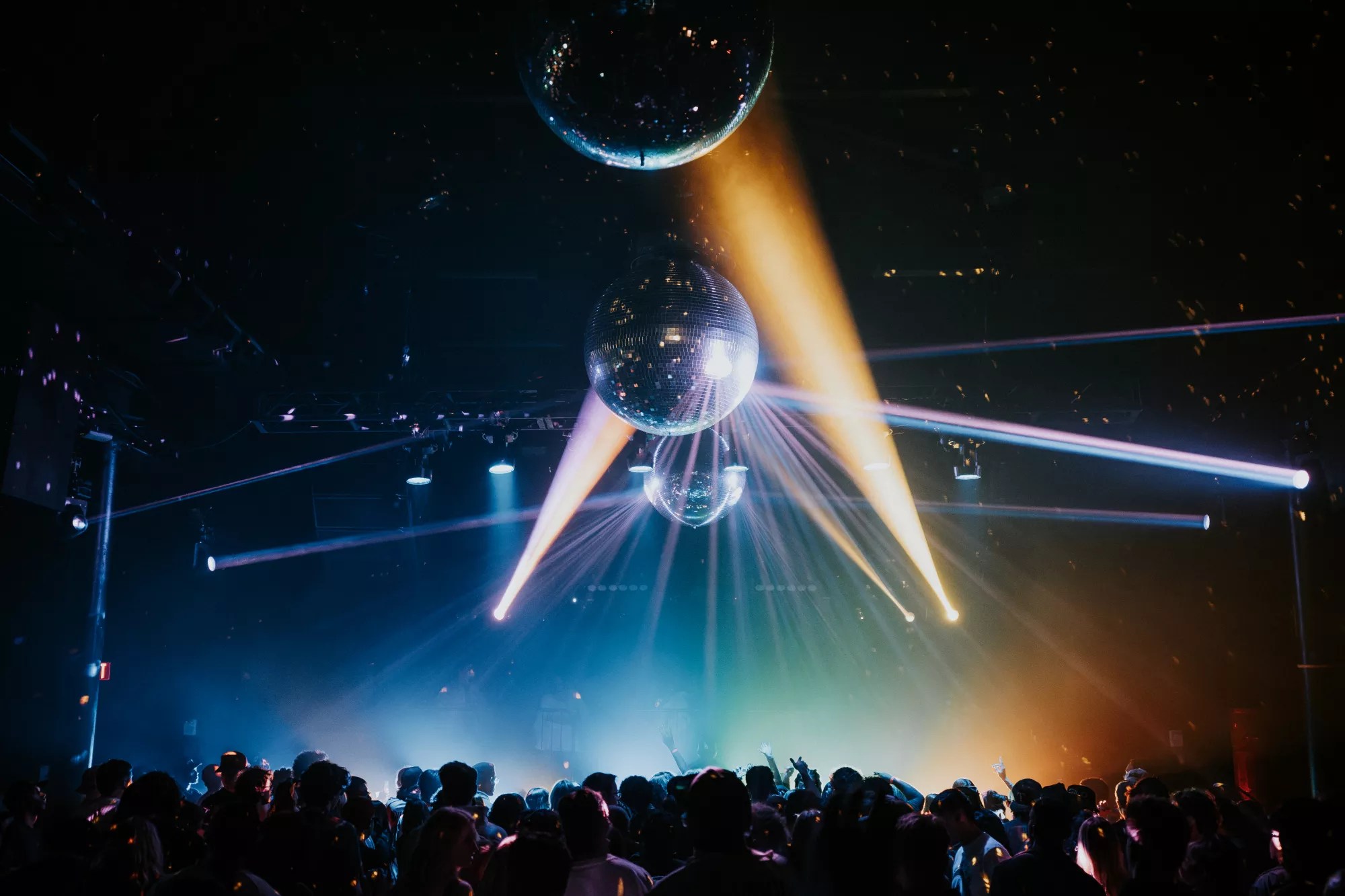 A crowd dances at a rave under disco balls.